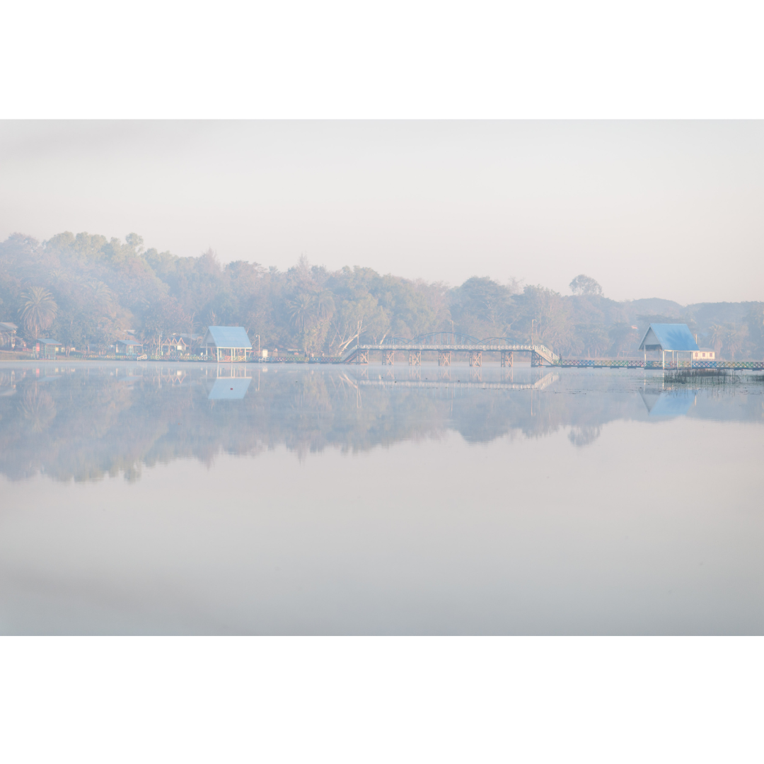 A lake with a tree line in the distance and smoke in the air